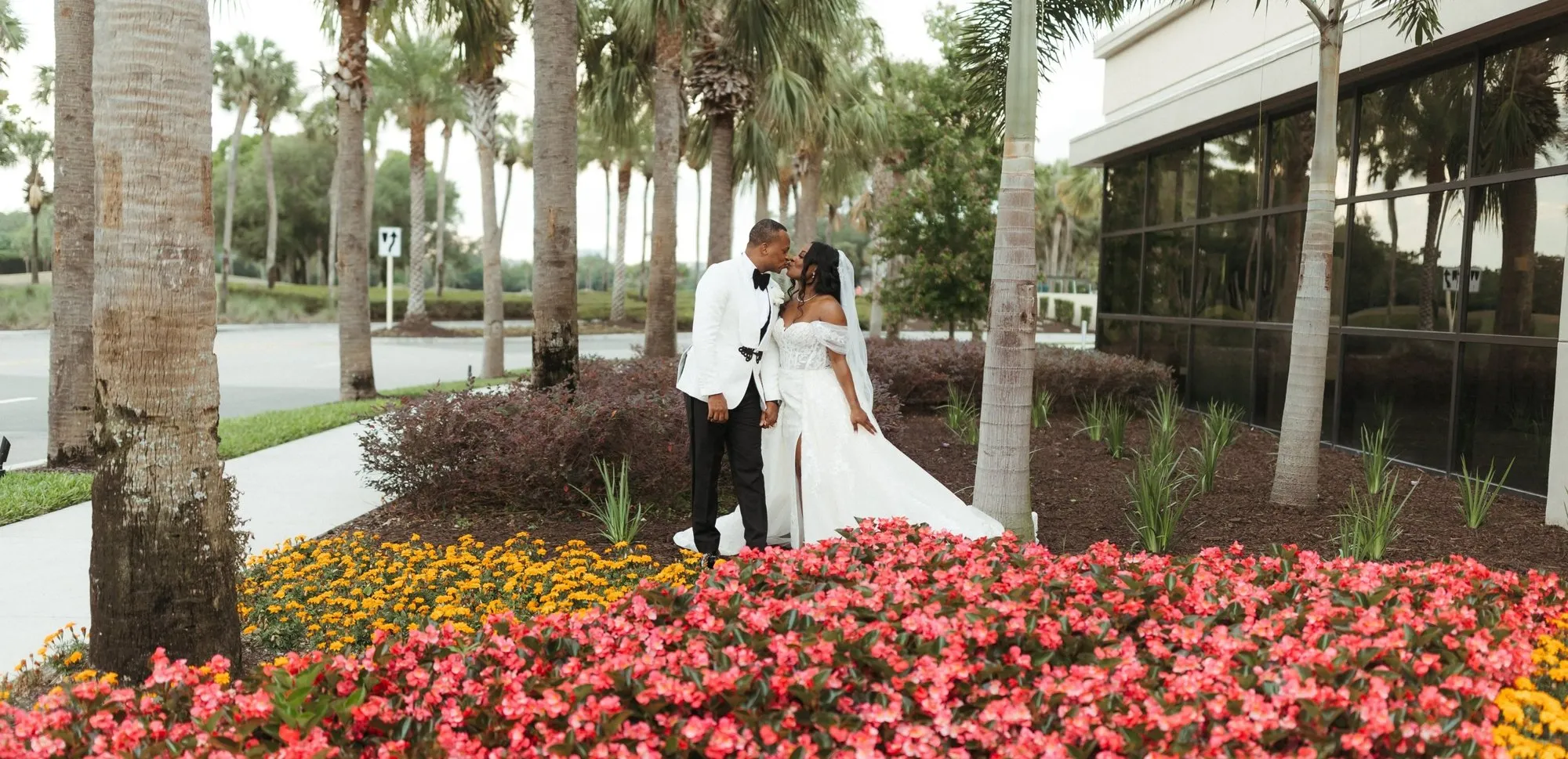 A newly married couple kissing between palm trees after their ceremony
